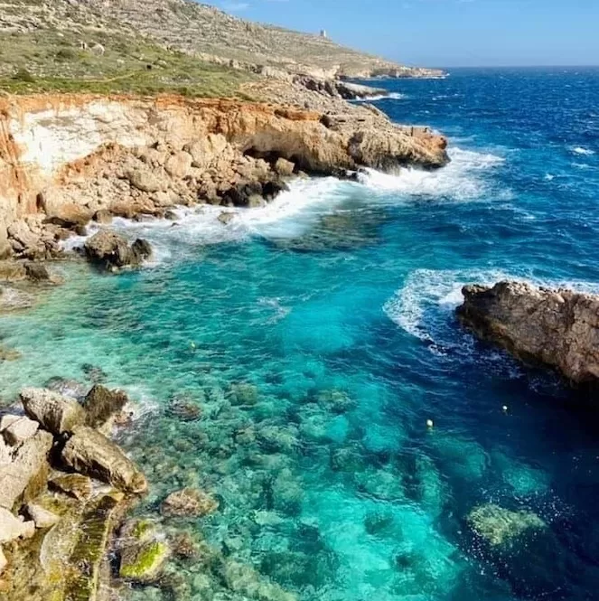 A stunning coastal scene with crystal-clear turquoise waters and rocky cliffs. The vibrant colours of the water contrast beautifully with the rugged rocks, creating a picturesque view. 