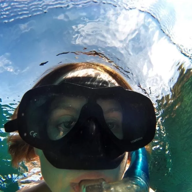 Close-up underwater view of a person wearing a snorkel mask and gazing into the clear blue water.