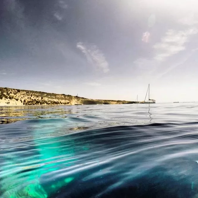 Scenic seascape while snorkelling in Malta, capturing the view of a sailboat anchored near a limestone coastline, seen from below the clear waters.