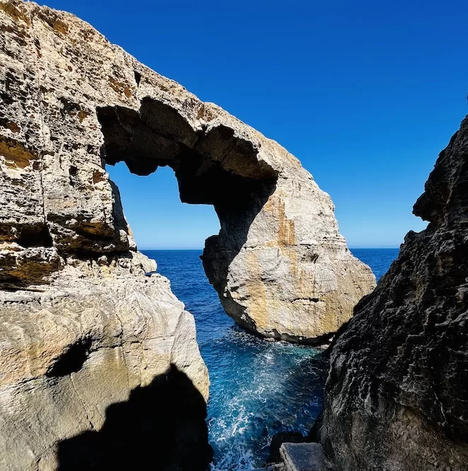 Standing tall against the blue sky and sea, the Wied il-Mielah in Gozo forms a natural arch between two rugged cliffs. The arch's majestic presence a stunning sight, showcasing the raw beauty of nature.