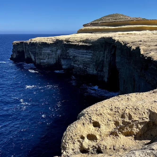 On the coastline, overlooking the deep blue sea, we see cliffs with caves along the hike from Wied il-Gasri Valley to the Wied il-Mielah.

