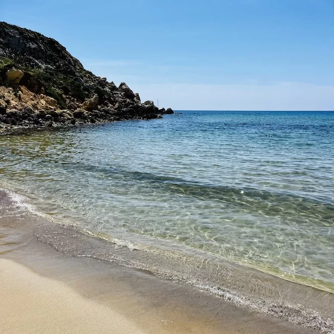 A scenic view of Golden Bay Beach with clear water gently lapping against the shore on a sunny day.