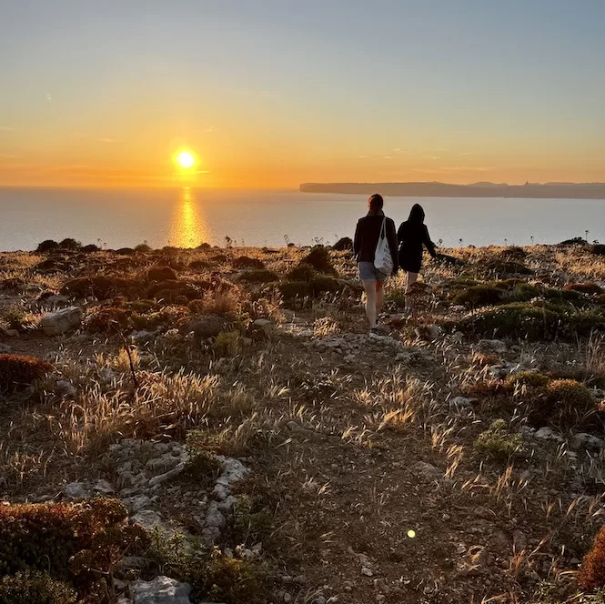 Two people walking hand in hand through a rugged landscape close to radar station in the Paradise Bay area during sunset by the sea.