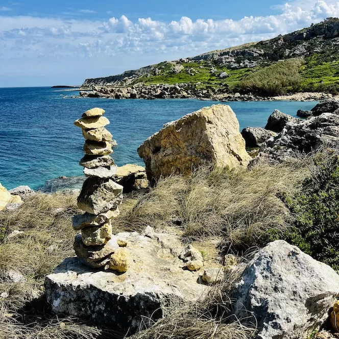 A stack of rocks against the coastal backdrop near Imġiebaħ Beach, Malta. The blue sea extends to the horizon.