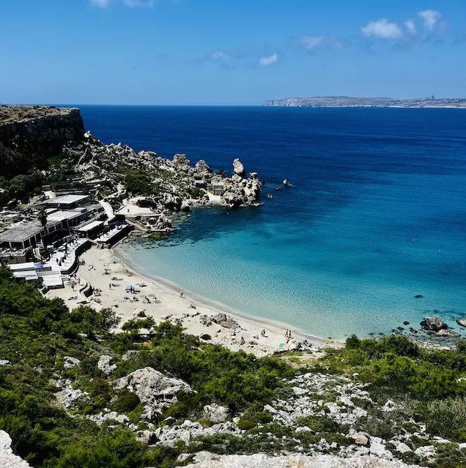 Aerial view of a picturesque Paradise Bay Beach surrounded by rocky cliffs, clear turquoise waters, and a sandy shoreline, bathed in sunlight.