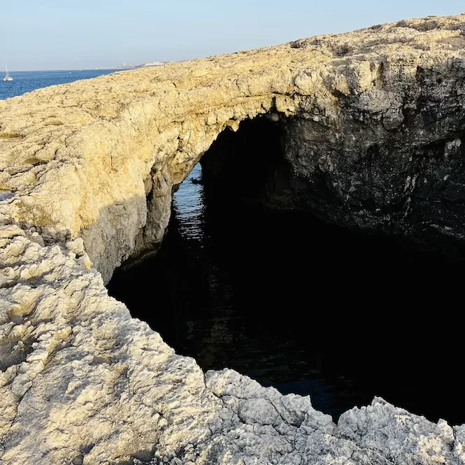 A natural rock formation resembling an arch over dark water, along a rugged coastline. This is Coral Lagoon's opening into the sea.