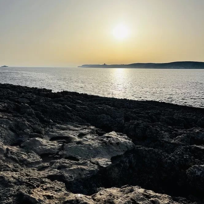 A rocky shore illuminated by the setting sun seen from Malta's Coral Lagoon.