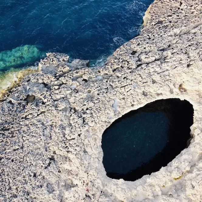 Aerial view of a rocky coastline with a deep circular cave of Coral Lagoon that looks like a pool of water formed in the limestone.