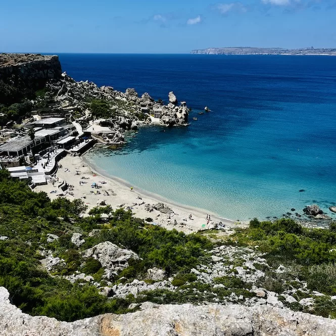 A picturesque sandy Paradise Bay Beach located between rugged cliffs, with crystal clear turquoise waters. Sunbathers relax on the shore while others swim in the inviting sea.