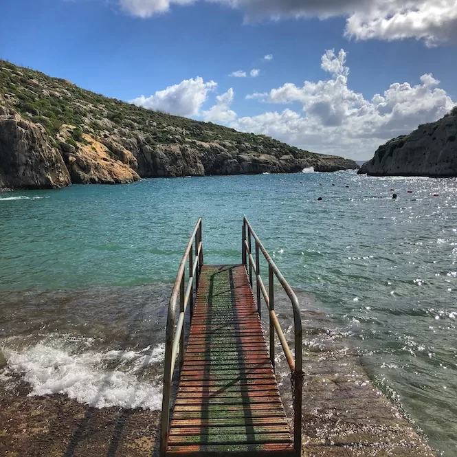 A scenic view of Mgarr Ix-Xini, a picturesque beach cove surrounded by rocky cliffs and clear turquoise waters. Visitors can enjoy swimming and snorkelling in this tranquil natural setting, making it a popular destination for beachgoers in Gozo.