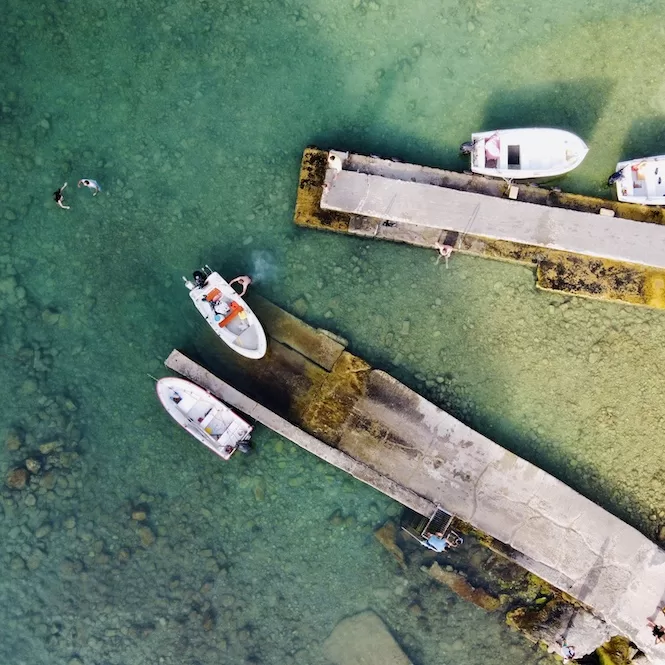 A bird's-eye view of fishermen's boats docked at the pier and people swimming in the  waters of the Inland Sea in Gozo. 