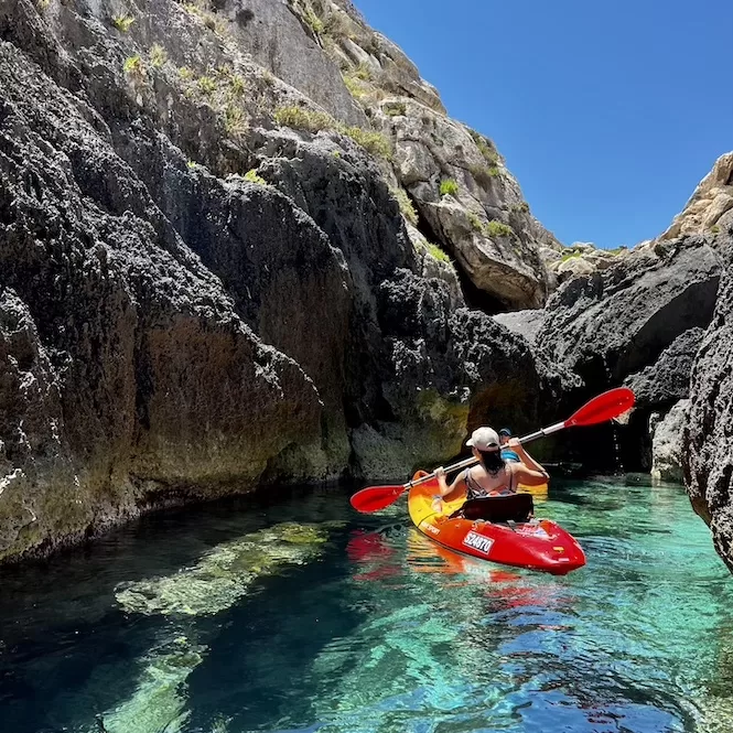 Kayaking through narrow inlets in Mgarr Ix-Xini Bay, the clear waters reveal the rocky formations beneath. 