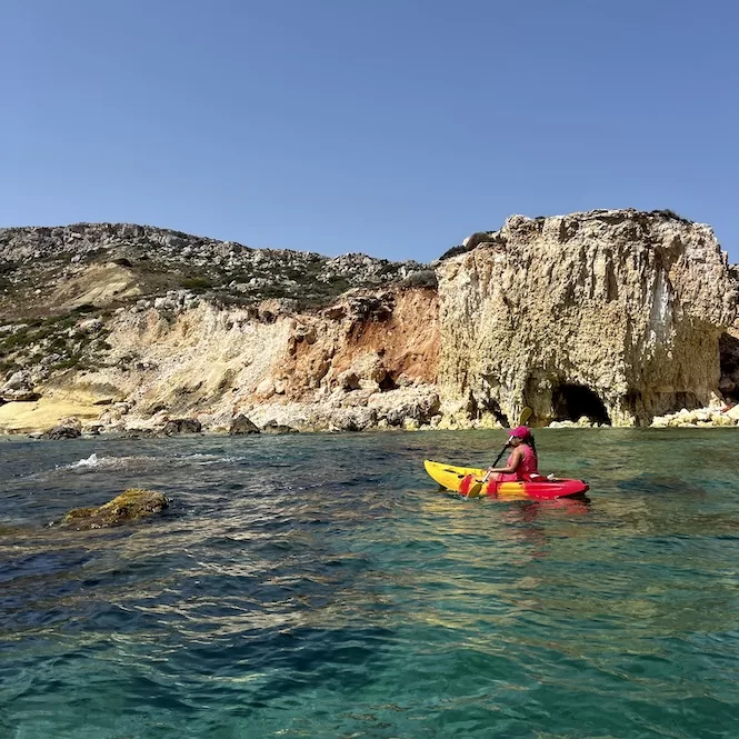 In Imgiebah Bay, Malta, a lone kayaker navigates the crystal-clear waters, surrounded by rugged cliffs and a majestic sea cave. The vibrant red kayak contrasts beautifully with the turquoise hues of the water.






