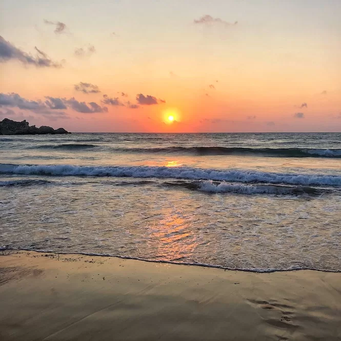 The sun setting over the serene waters of Golden Bay in Malta, painting the sky with warm hues of orange and pink.