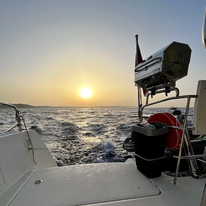 The sun setting over the horizon, casting a warm glow across the open sea from the deck of a boat. Enjoying a peaceful evening on the water, witnessing the beautiful sunset while sailing.