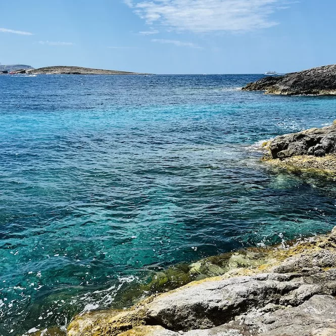 Rocky coastline on the right side of Hondoq Bay in Gozo, Malta, with clear blue waters stretching to the horizon.