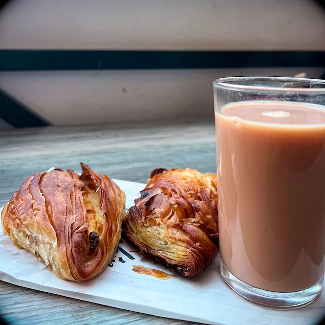 A plate with two pastizzi, a traditional Maltese pastry, alongside a glass of tea. Pastizzi are a popular and affordable food in Malta, typically filled with either ricotta cheese or mushy peas.