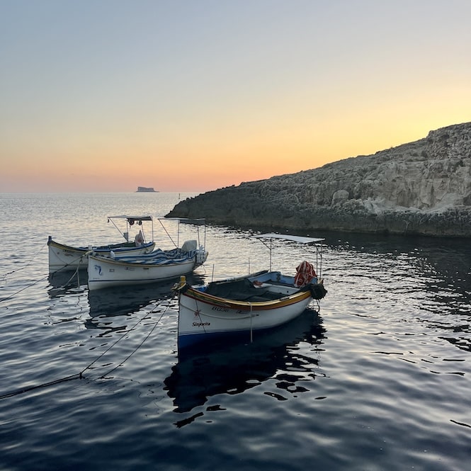 Fishing boats anchored near the rocky coastline at sunset at Blue Grotto in n Malta.