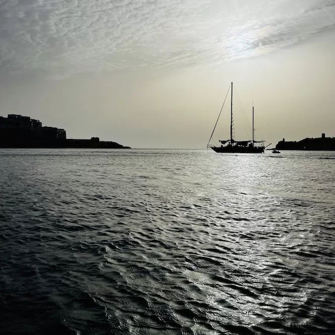 Morning views from a paddle board - a sailboat anchored in calm waters with the silhouette of buildings in the background. This image captures the tranquility of the sea and the beauty of the sunrise.