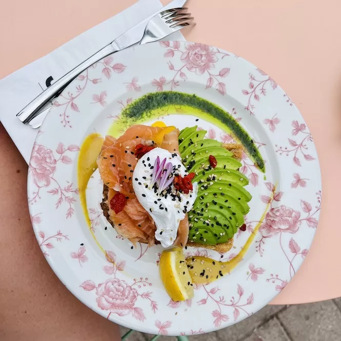 A delicious brunch plate at Java in Naxxar featuring smoked salmon, poached egg, avocado slices, lemon wedges, and chia seeds, drizzled with green pesto sauce.