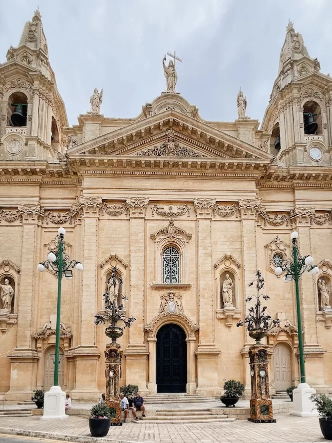 A view of the Parish Church in Naxxar, Malta, showcasing its impressive facade adorned with statues and ornate architectural details.