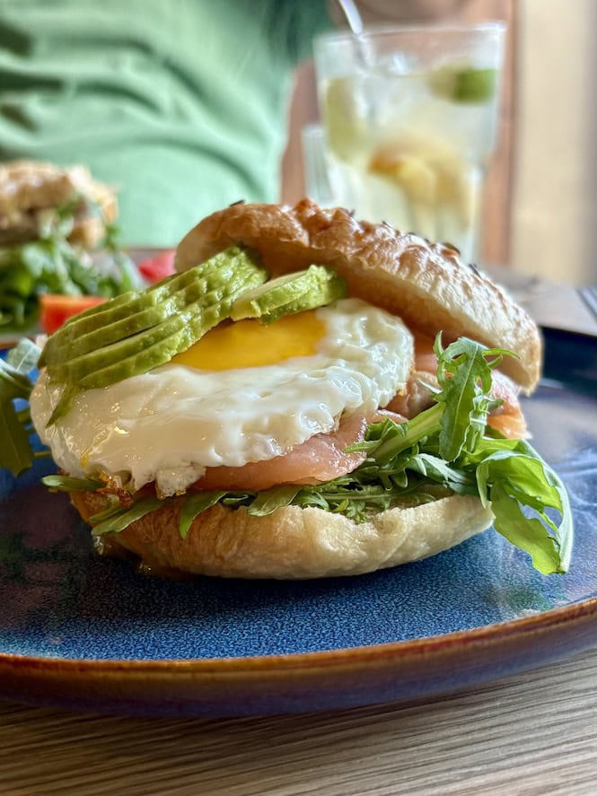 Crispy sandwich with fried egg, avocado slices, lettuce, and a side of refreshing drink in Malta.