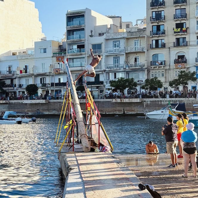 Participant sliding off the greasy pole during the ġostra competition at the village feast in Malta, a lively summer tradition.