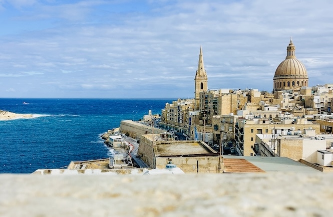 A picturesque view captured during a Valletta walking tour, featuring the stunning cityscape with iconic church dome against the backdrop of the Mediterranean Sea. The historic buildings line the coastline, showcasing the rich architectural heritage of Valletta.