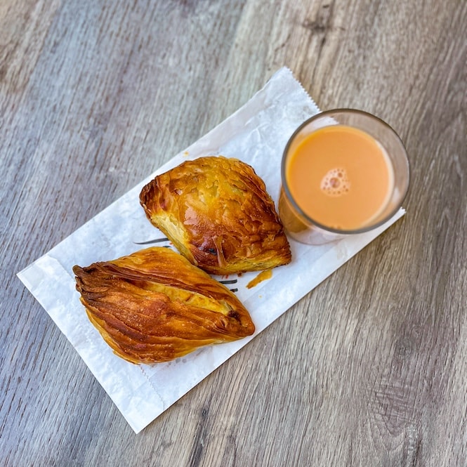 A close-up view of traditional Maltese pastizzi, with its flaky, golden-brown pastry on a white napkin, paired with a glass of tea with milk on a wooden surface. This image epitomizes a typical Maltese snack, enjoyed on a Valletta walking tour.