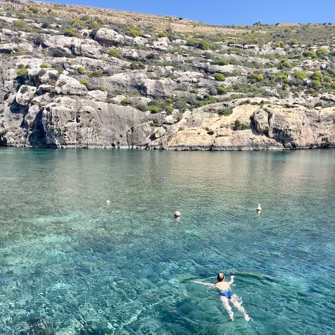 A woman swimming in crystal-clear waters at Mgarr Ix-Xini, Gozo.