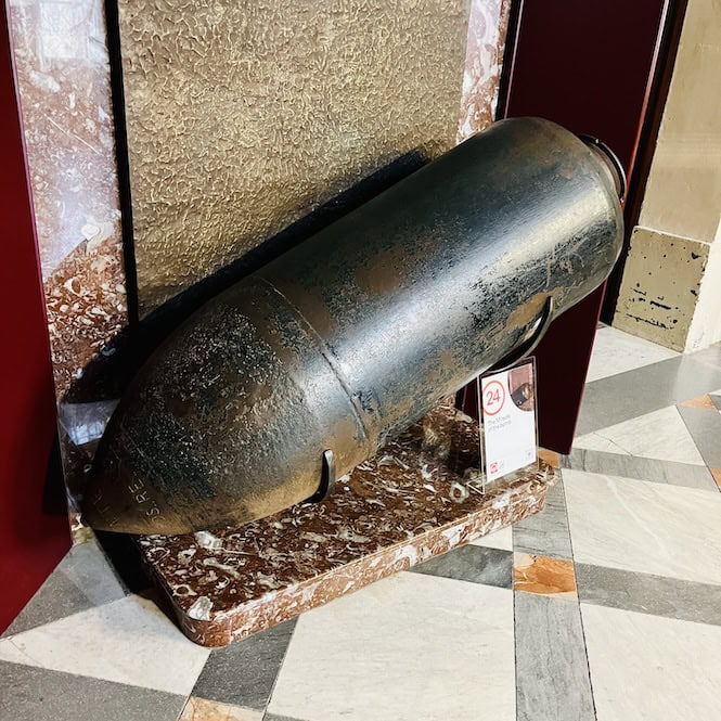 A replica of the World War II bomb that pierced the Mosta Dome without exploding, displayed on a marble pedestal inside the church, serving as a poignant reminder of the miraculous event that spared hundreds of lives.