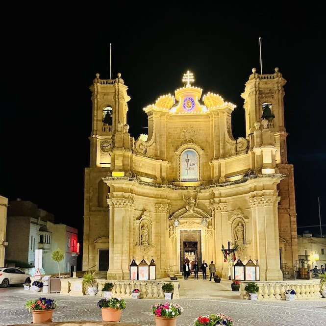 Illuminated baroque facade of the Church in the main square of Gharb village, Gozo, Malta at night.