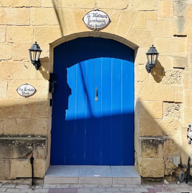Blue wooden door of a traditional Gozo farmhouse in Gharb village, adorned with signs.