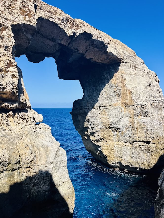  Wied il-Mielaħ natural limestone arch framing blue sea along the dramatic cliff coastline of Gozo island, Malta.