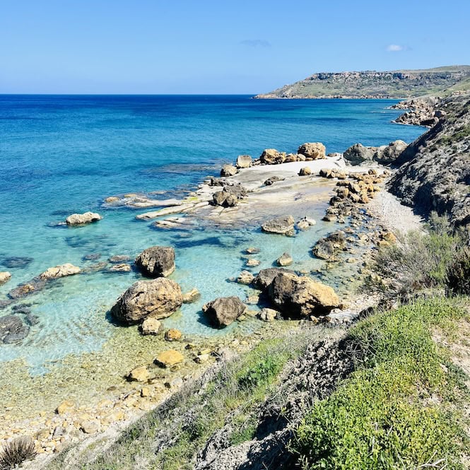 A small, rocky beach in Gozo with white rock formations and clay cliffs.