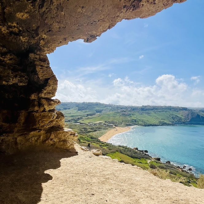 Tal Mixta Cave overlooking Ramla Bay. The cave looks like a window into a green bay and a beach with orange sand.
