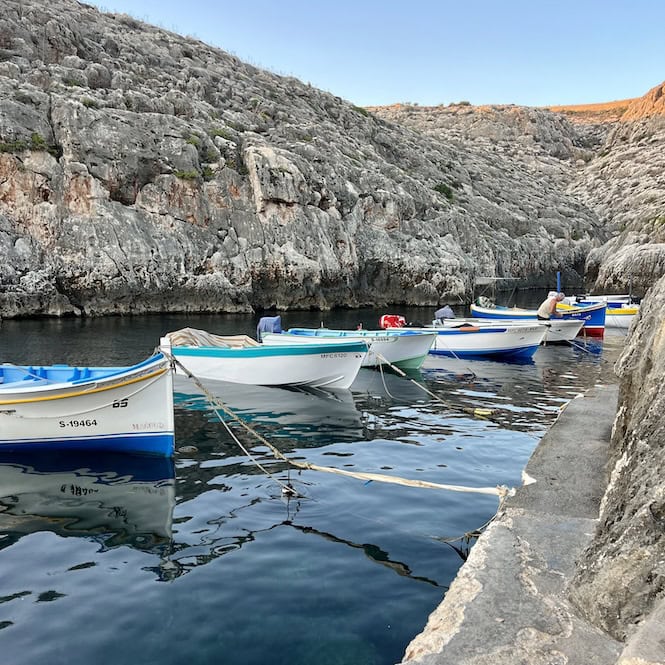 Colorful fishing boats docked in a rocky cove in Malta, highlighting the island's picturesque coastal scenery in September.