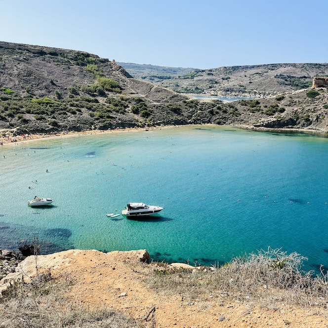 Boats anchored in the crystal clear blue waters of Golden Bay Bay in Malta, an ideal destination in September.