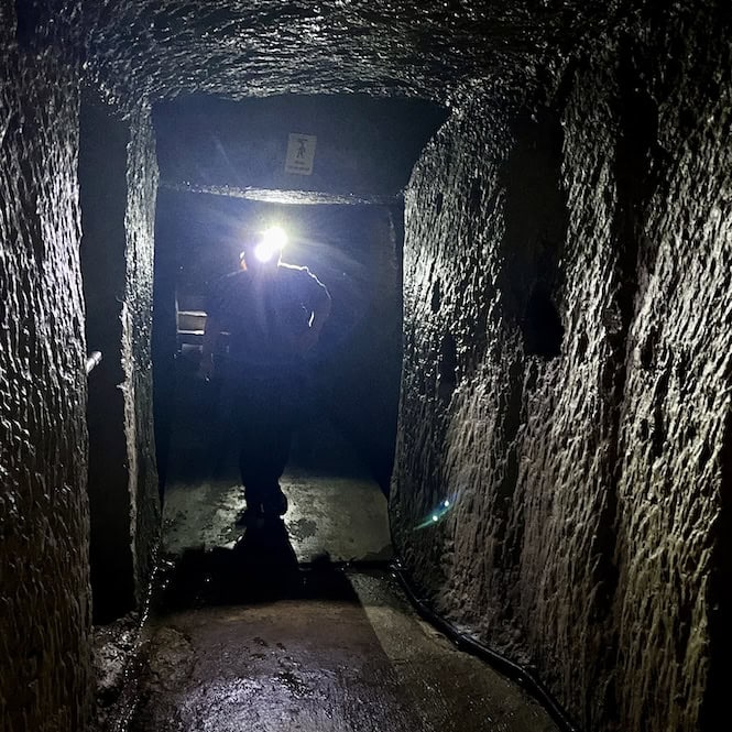 A person wearing a helmet with a flashlight exploring a dark tunnel in Underground Valletta.

