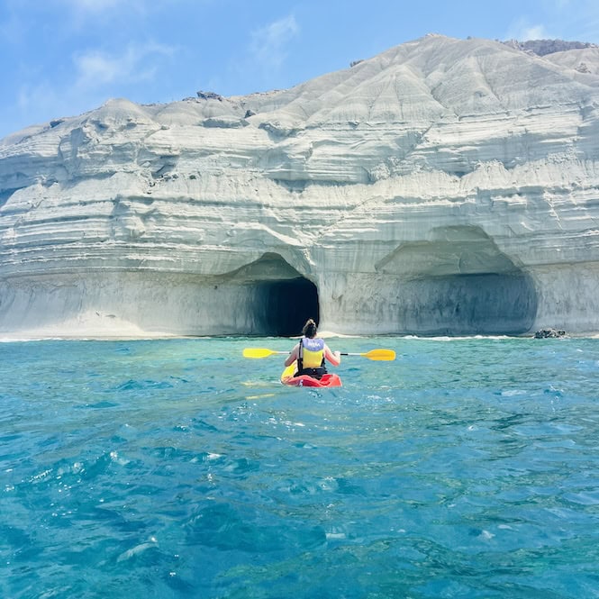 A person kayaking towards the stunning Ta' Marija Cave near Gnejna Beach, with its unique rock formations visible in the background.