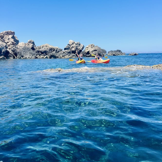 Two kayakers enjoying the crystal clear waters near next to the rocky coast of Gnejna Beach.