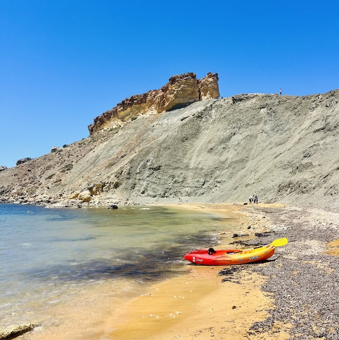 A colorful kayak rests on the sandy shore, with the stunning clay cliffs in the background.