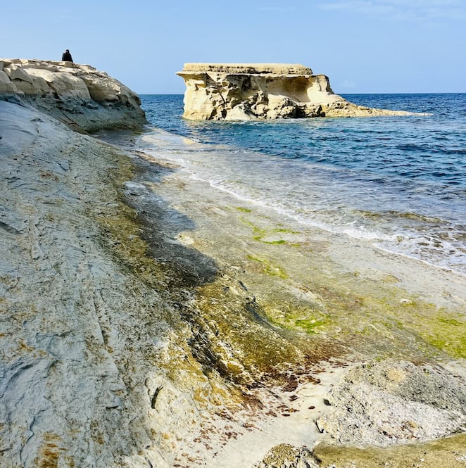 A scenic view of eroded coastal rock formations along the shore in Marsalforn, Gozo, with blue sea water in the foreground.