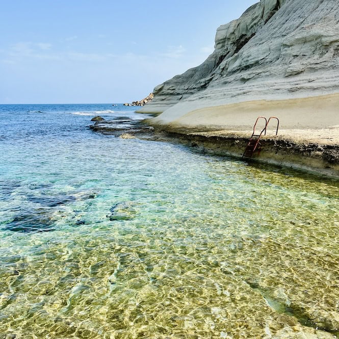 Clear shallow waters and rocky coast of Għar Qawqla Beach in Marsalforn, Gozo
