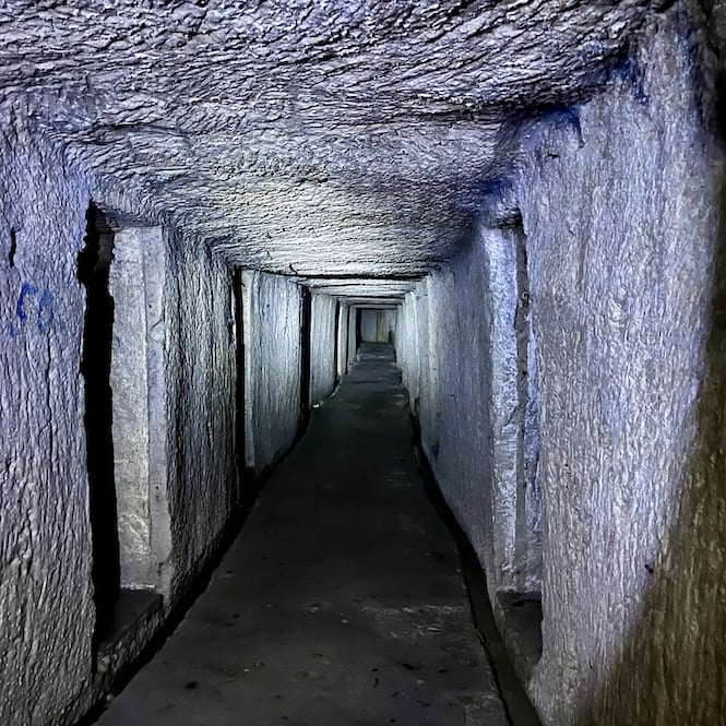 A long, dimly lit tunnel in Underground Valletta with multiple entrances to smaller rooms.