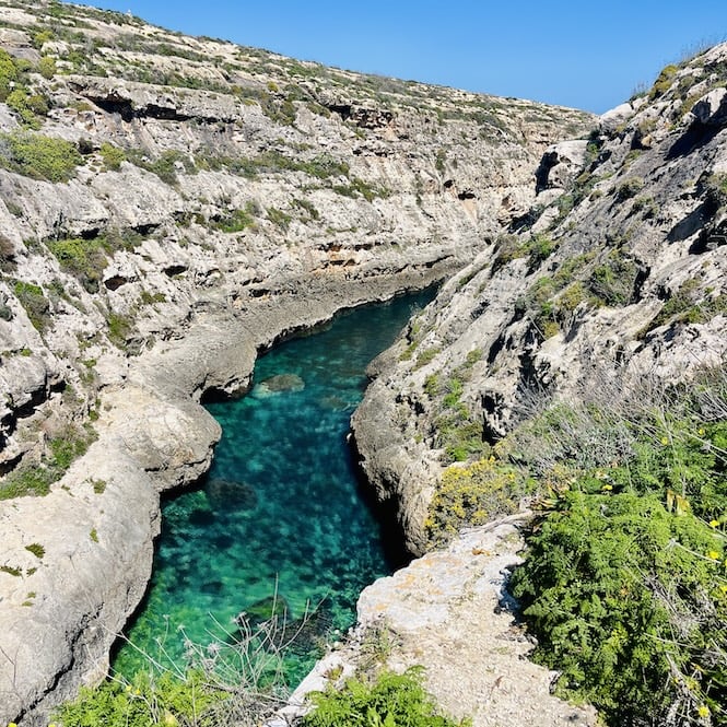 A narrow valley of Ghasri with clear turquoise water that winds through rocky cliffs on the island of Gozo. Ghasri Beach is one of the hidden beaches in Gozo