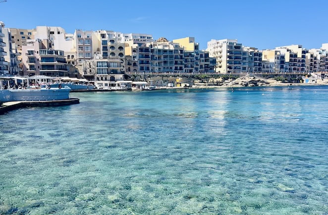Apartment buildings line the shore of the crystal-clear blue waters in Marsalforn Bay, Gozo, Malta
