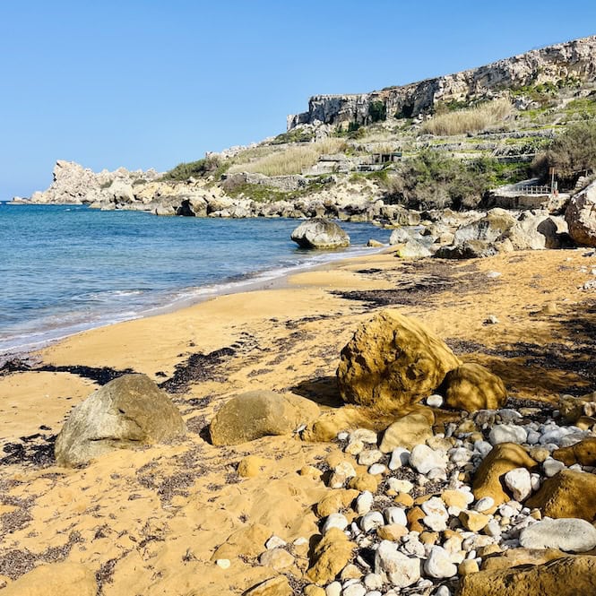 San Blas Beach, one of Gozo's hidden gems, showcases a picturesque cove with reddish sand, crystal-clear waters, and dramatic cliffs. The unspoiled natural setting, featuring rocky outcrops and sparse vegetation, adds to the beach's rustic appeal, making it a perfect escape for those seeking a tranquil and less crowded Gozo beach experience.