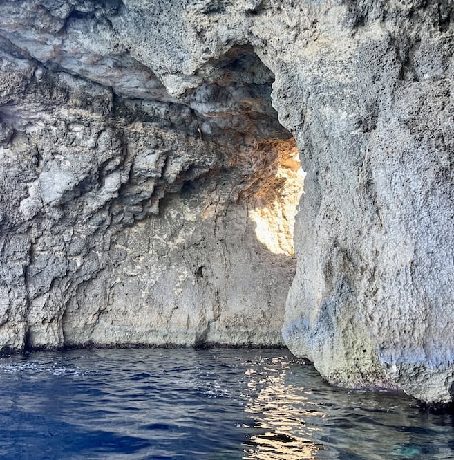 Sunlight illuminating the rocky cliffs inside the Blue Lagoon sea cave in Malta.
