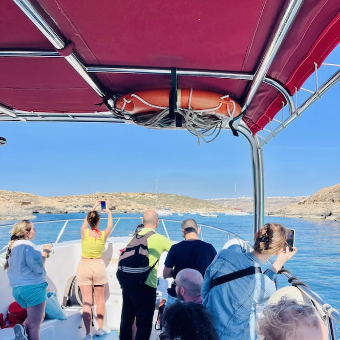 Small boat with pink sunroof filled with people on their way to Comino Island, Malta